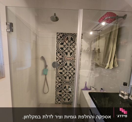 מקלחת עם ראש מקלחת, דלת זכוכית ודוגמת אריחים.